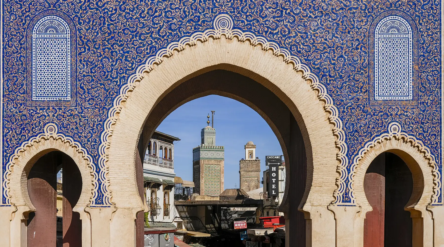 Bab Bou Jeloud-porten i Fes, dækket af blå zellij-fliser, indrammer minareten på Bou Inania-madrasaen.